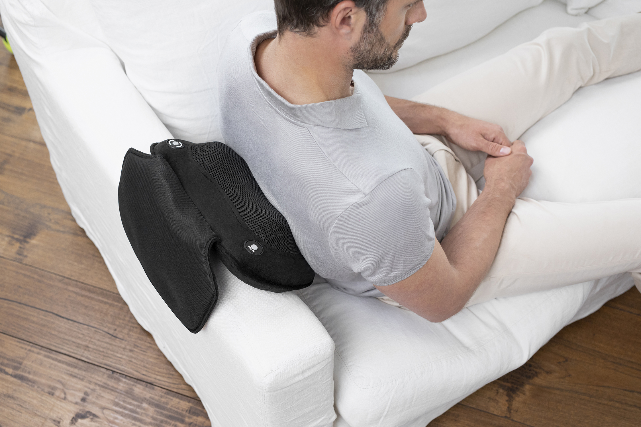 Man zit op een witte bank en gebruikt een zwart rugsteunkussen. Het kussen is ergonomisch ontworpen.