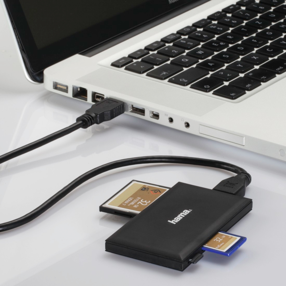 A laptop connected to a black card reader with SD and micro SD cards inserted, on a white surface.