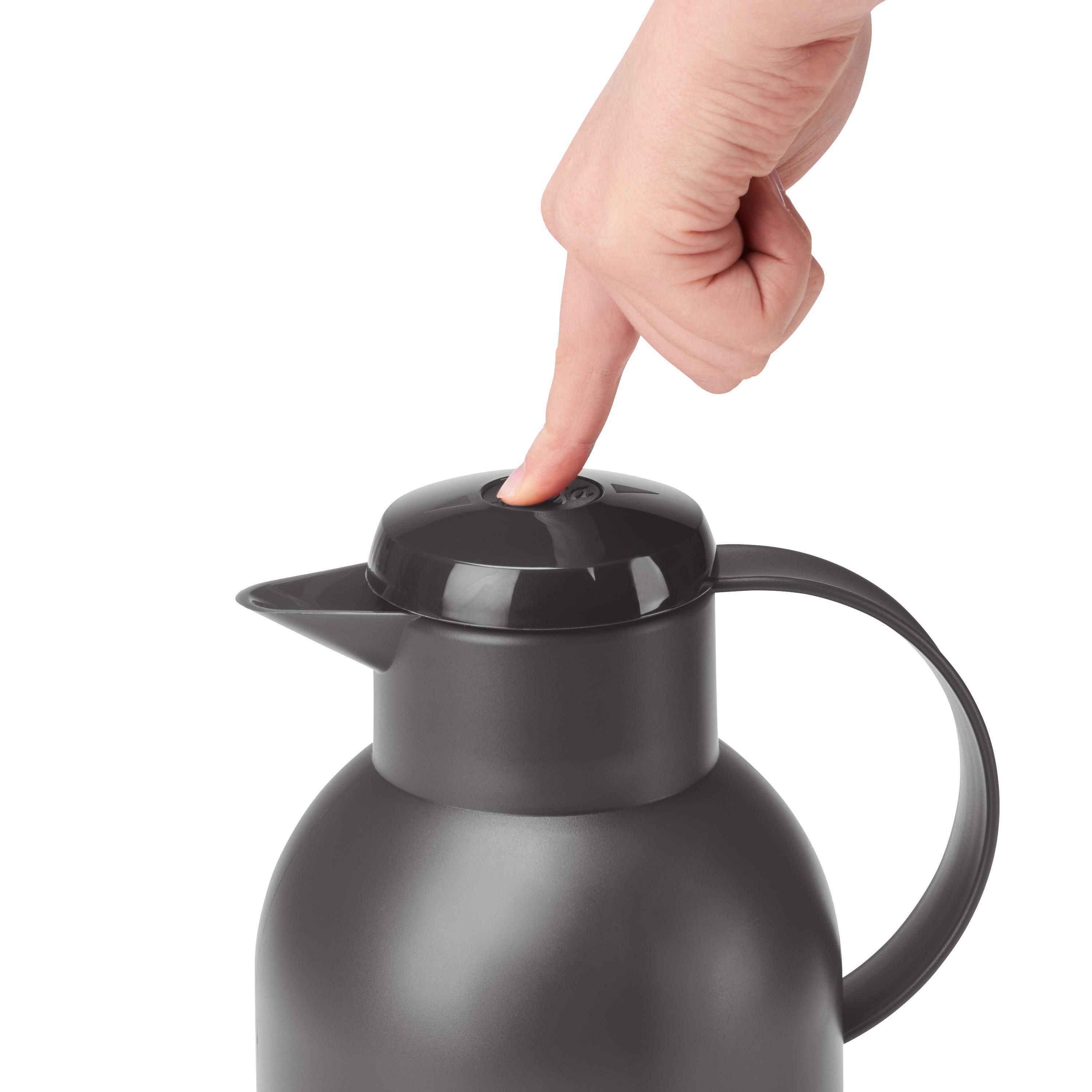 Hand drückt einen Knopf auf einer dunkelgrauen Thermoskanne. Weißer Hintergrund. Schwarzer Deckel und Griff.
