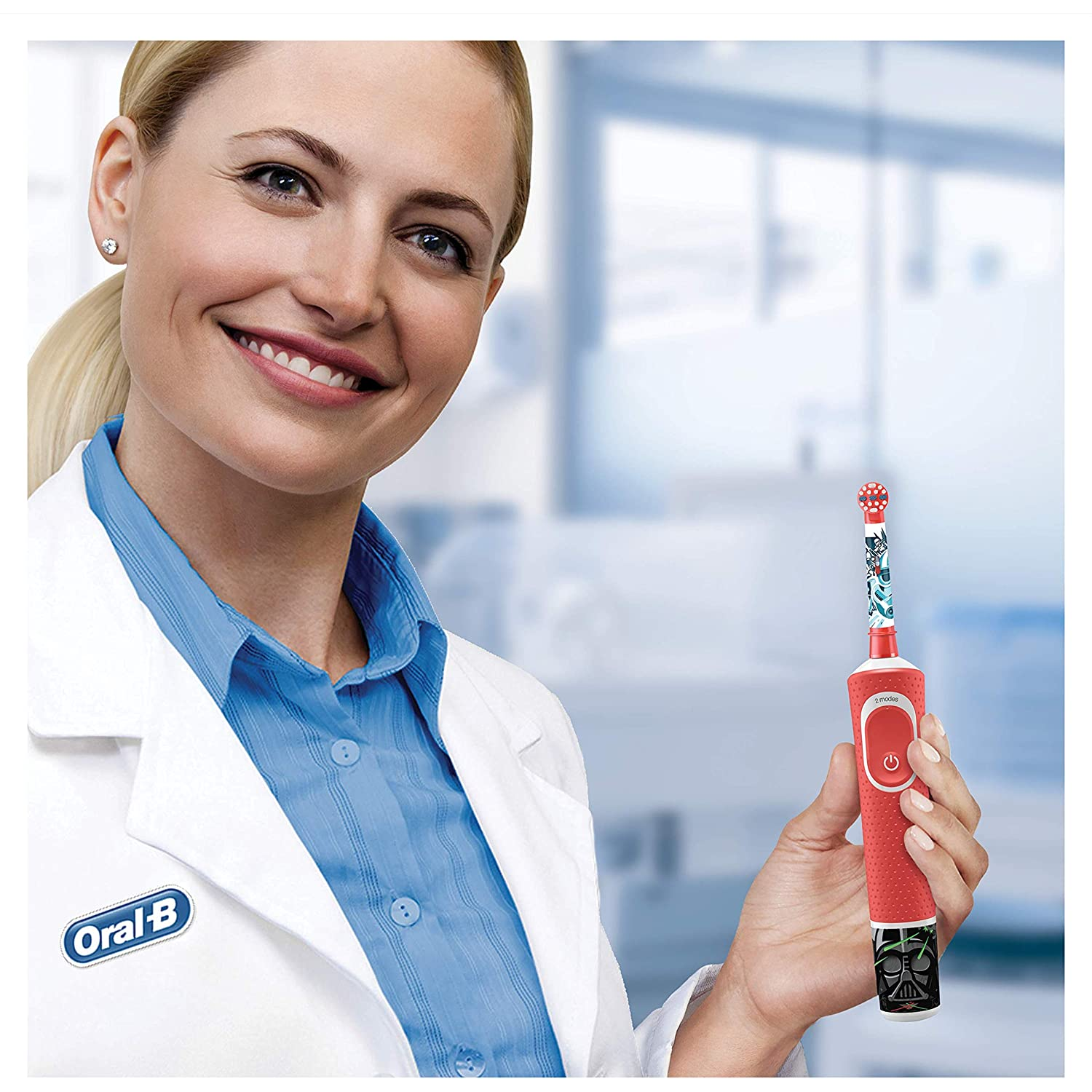 Una mujer sosteniendo un cepillo de dientes Oral-B rojo. Sonríe y lleva una bata de laboratorio.