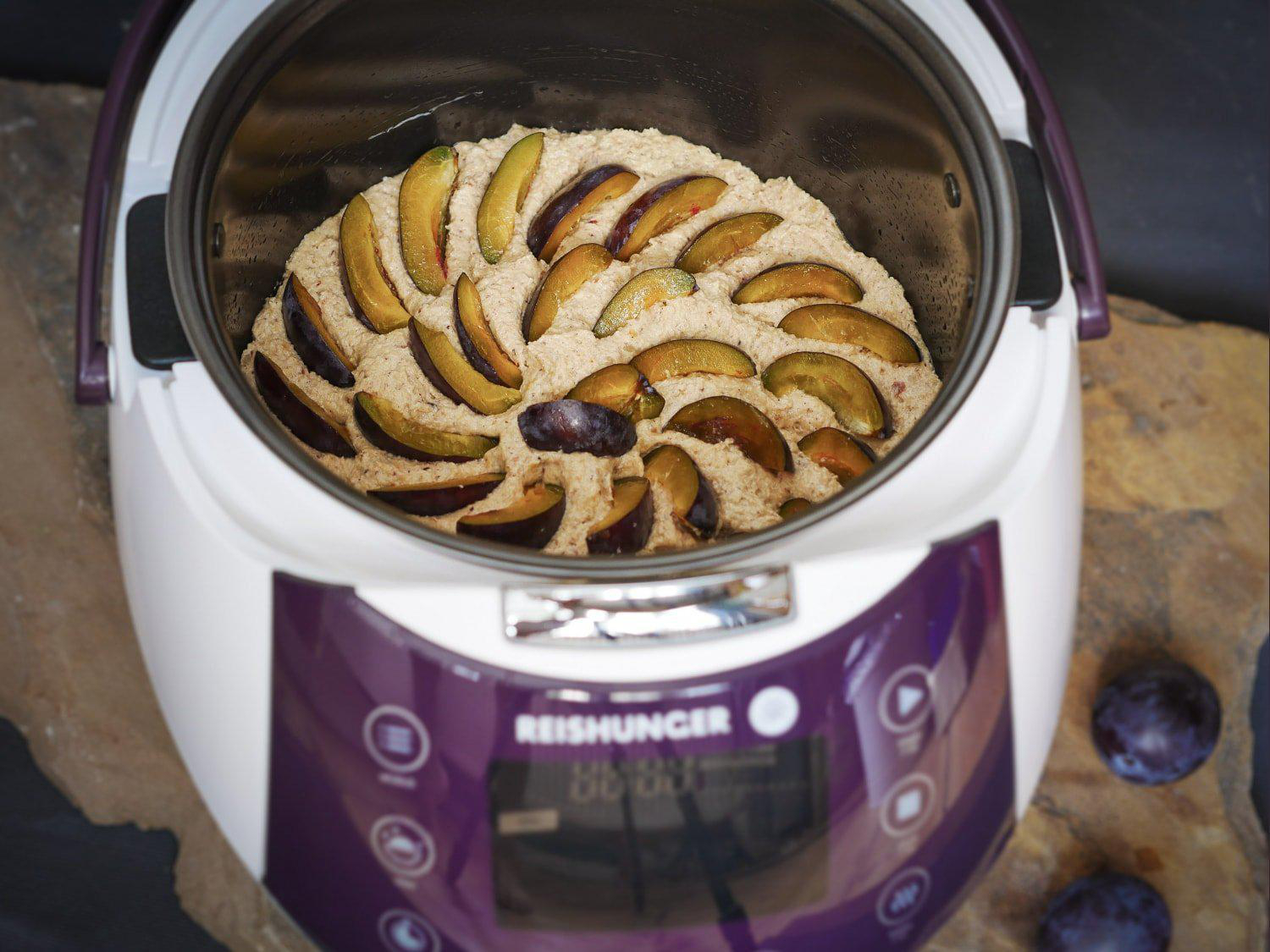 Ein Brotbackautomat mit Pflaumenkuchen darin, auf Holzoberfläche.
