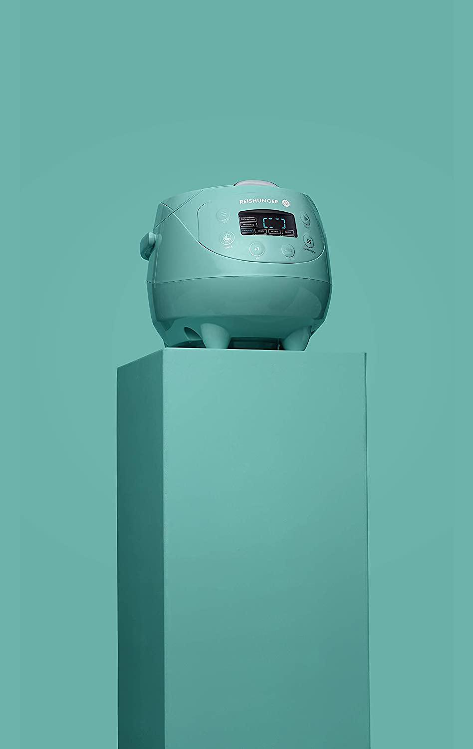 Ein mintgrüner Reiskocher auf einem mintgrünen Podest. Der Hintergrund ist ebenfalls mintgrün.