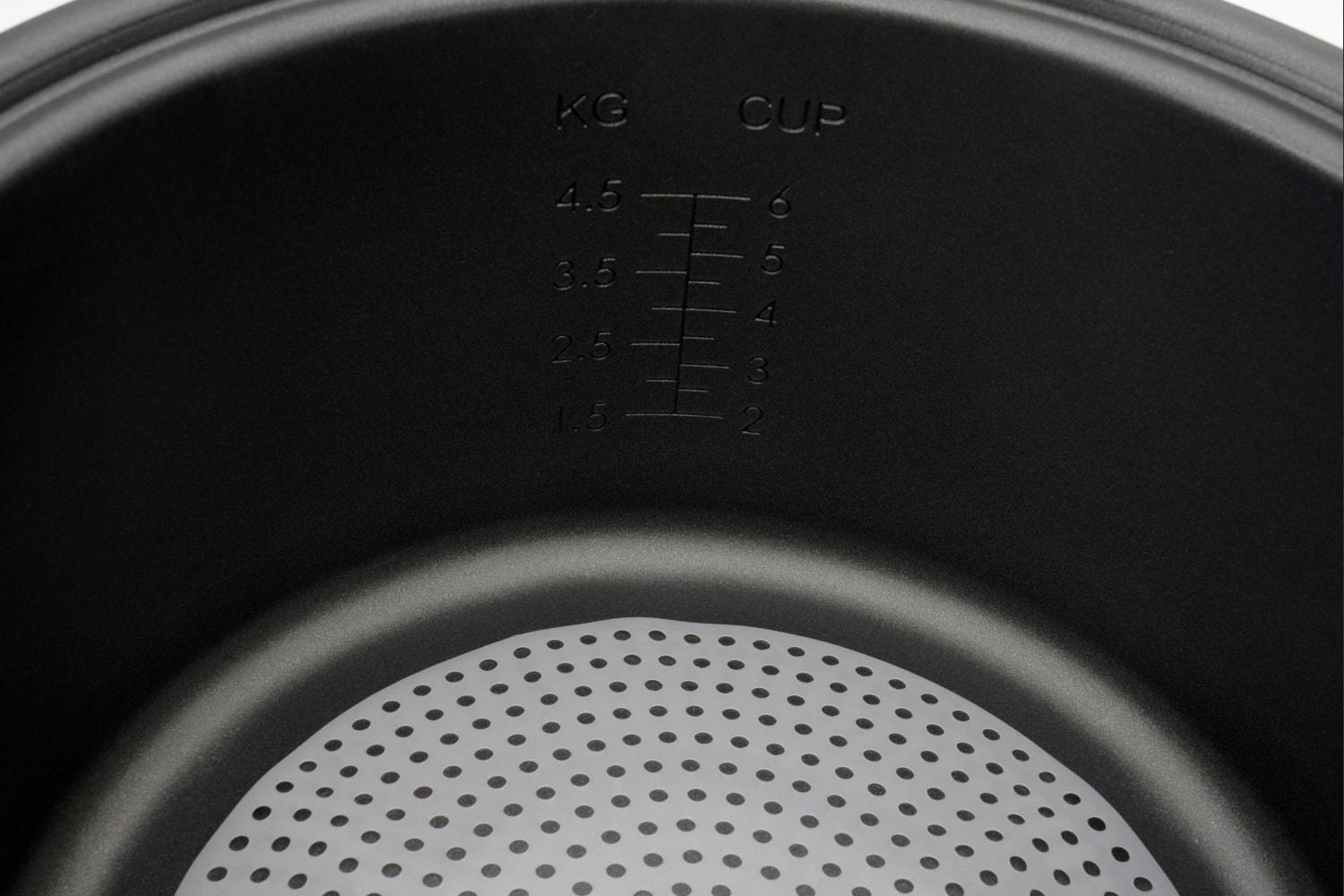 Innenraum eines schwarzen Topfes mit Messmarkierungen. Weiße perforierte Platte am Boden.