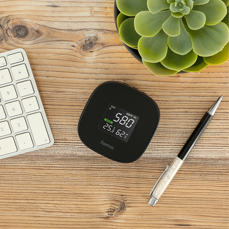 Zwarte CO2-monitor toont 580 ppm op houten bureau.