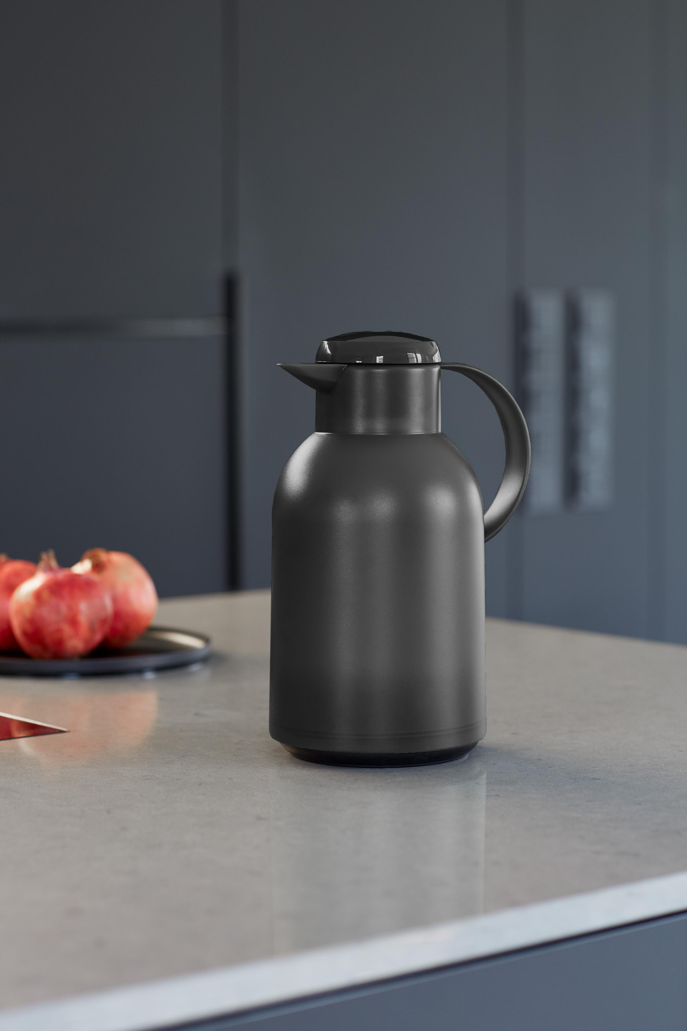 Eine schwarze Karaffe auf einer Arbeitsplatte, mit Granatäpfeln und verschwommenem Hintergrund.