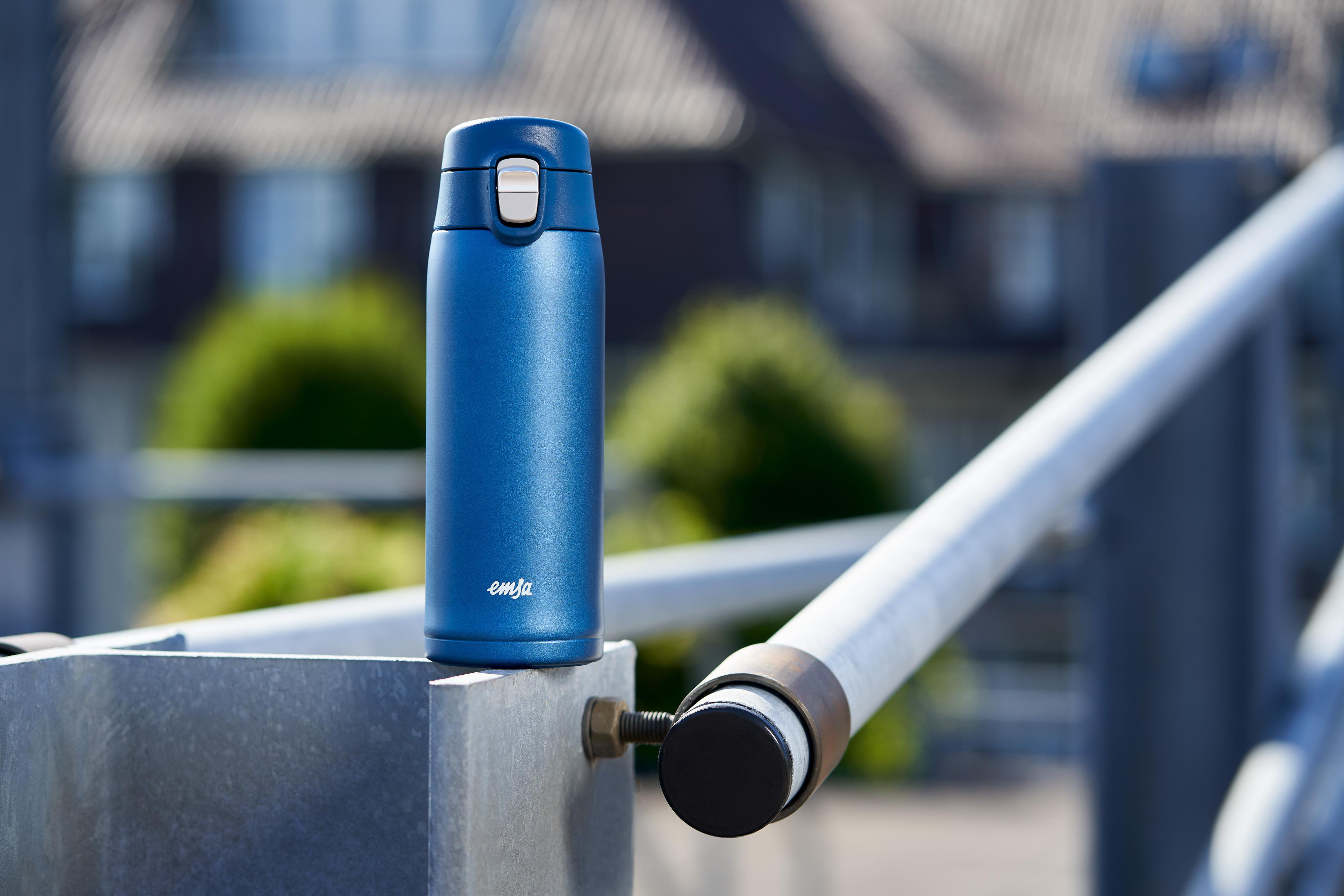 Blaue Isolierflasche auf einem Metallzaun. Weißer Deckel und Knopf. Emja-Marke.
