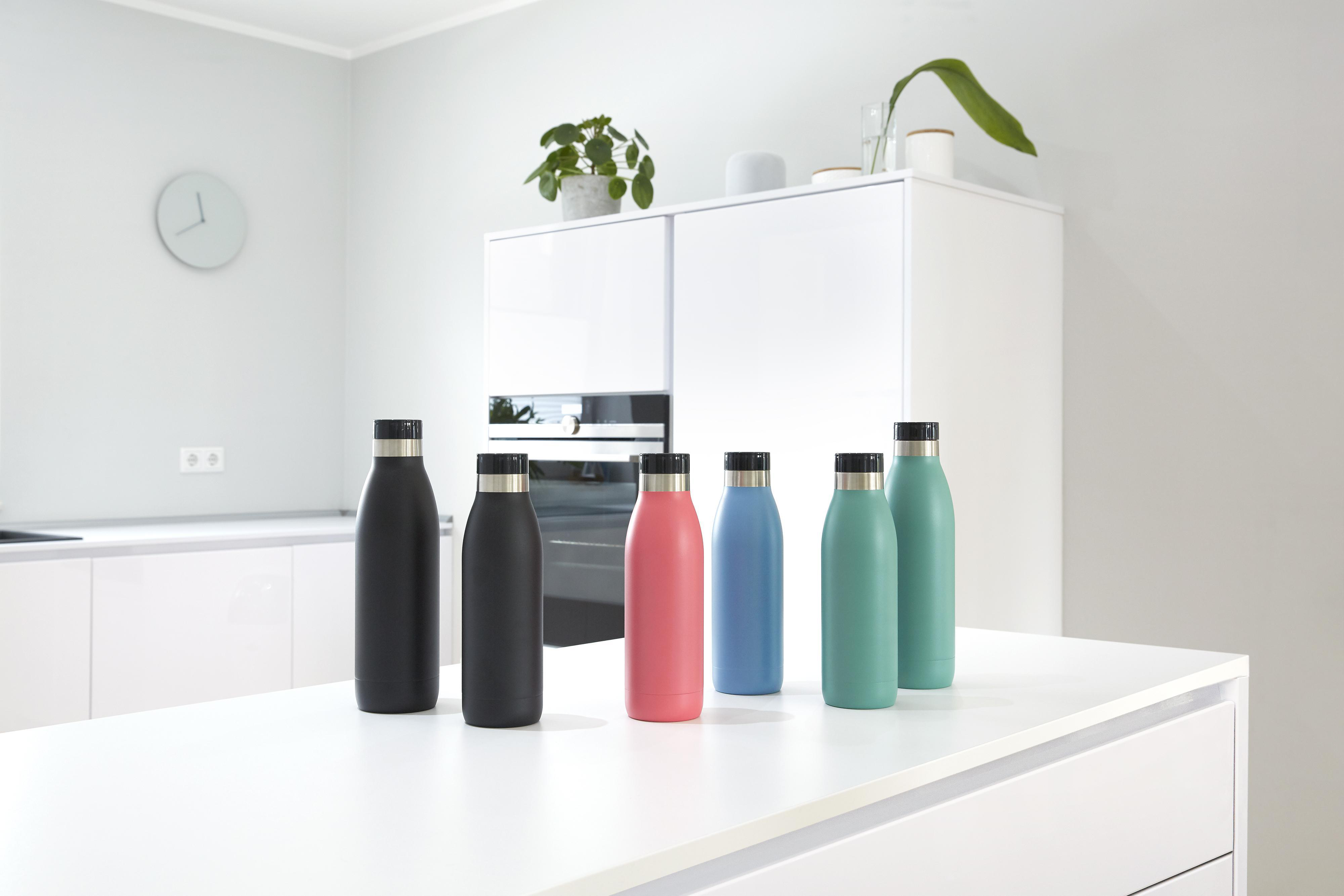 Auf einer weißen Küchentheke stehen sechs Wasserflaschen in verschiedenen Farben: schwarz, rosa, blau und zwei Grüntöne.