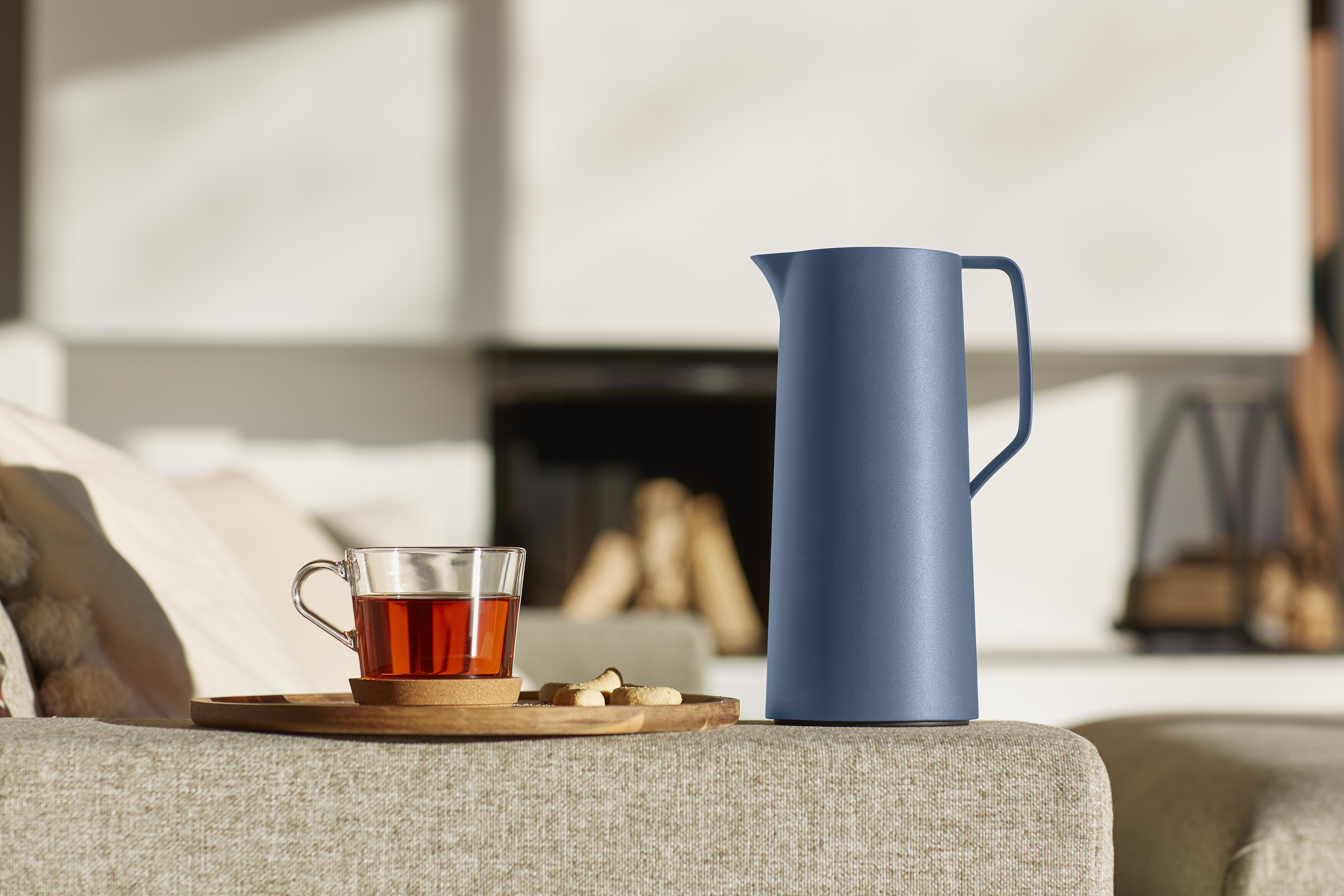 Blaue Thermoskanne und eine Tasse Tee auf einem Holztablett, ein Sofa und ein Kamin.