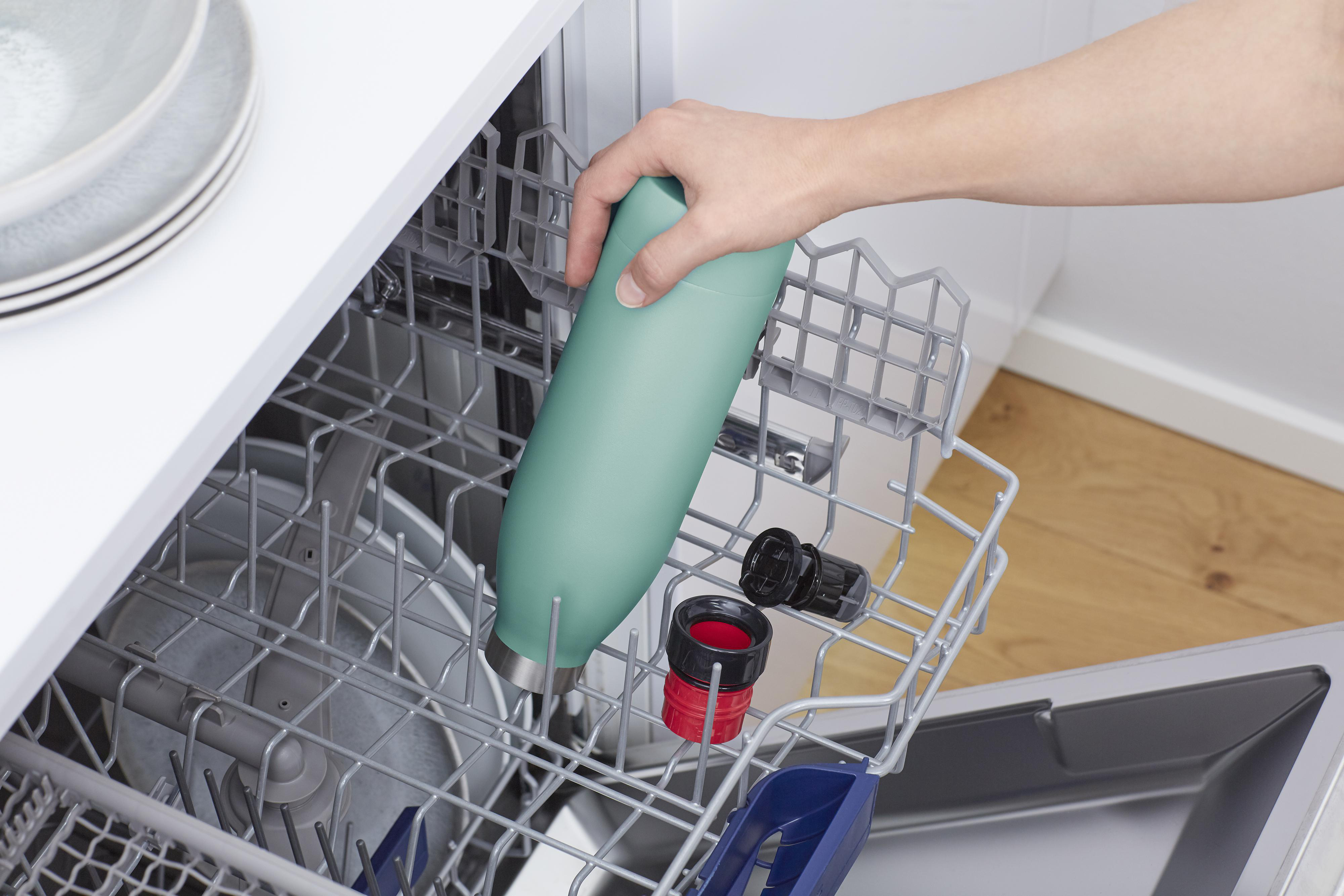 Hand, die eine grüne Wasserflasche in den Geschirrspüler legt.
