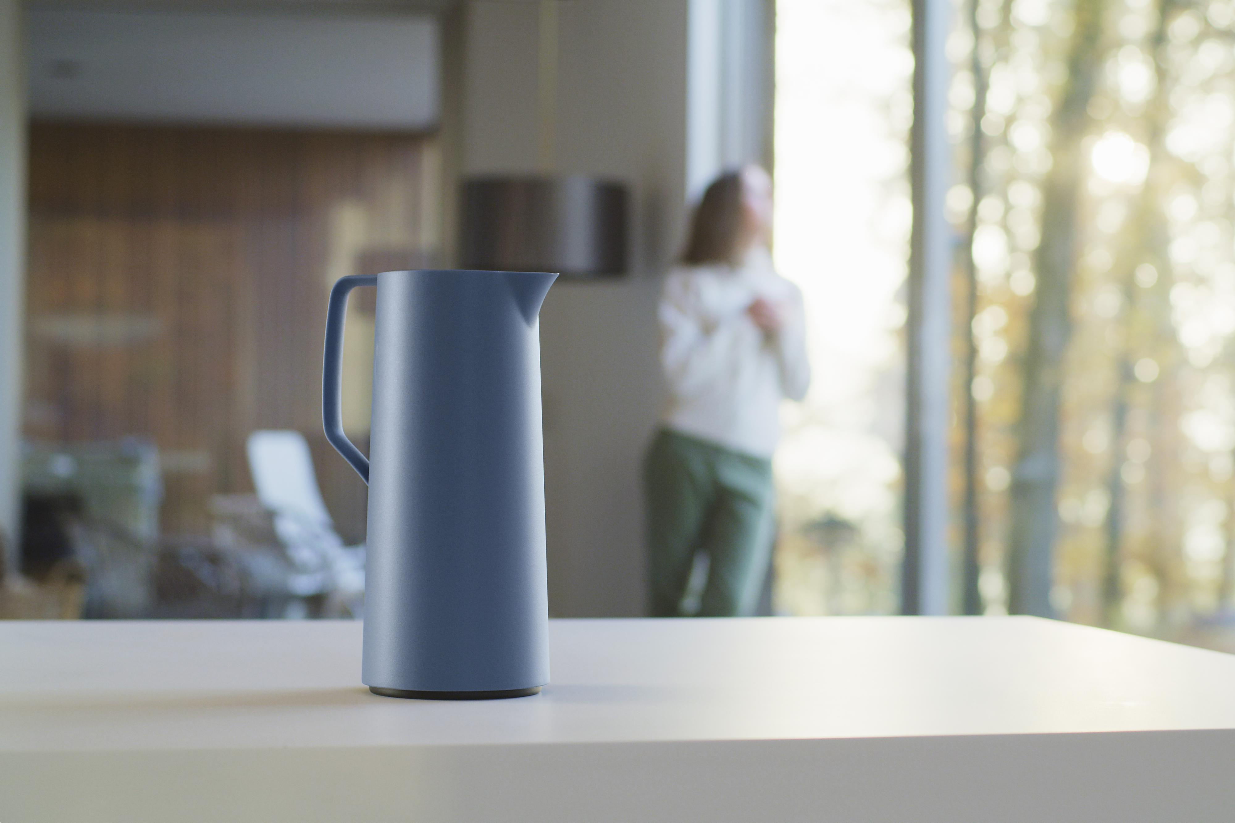 Ein blauer Wasserkrug auf einer weißen Arbeitsplatte. Verschwommener Hintergrund mit einer Frau am Fenster.