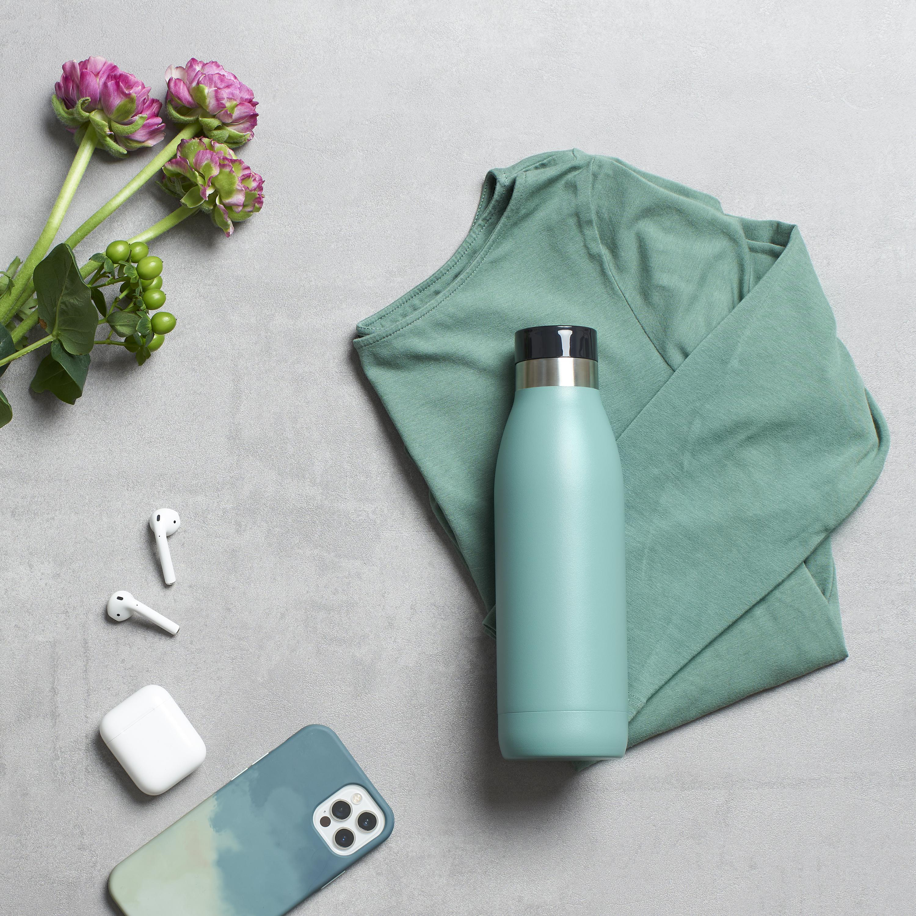Wasserflasche, Hemd, Telefon und Ohrhörer auf grauer Oberfläche mit Blumen.