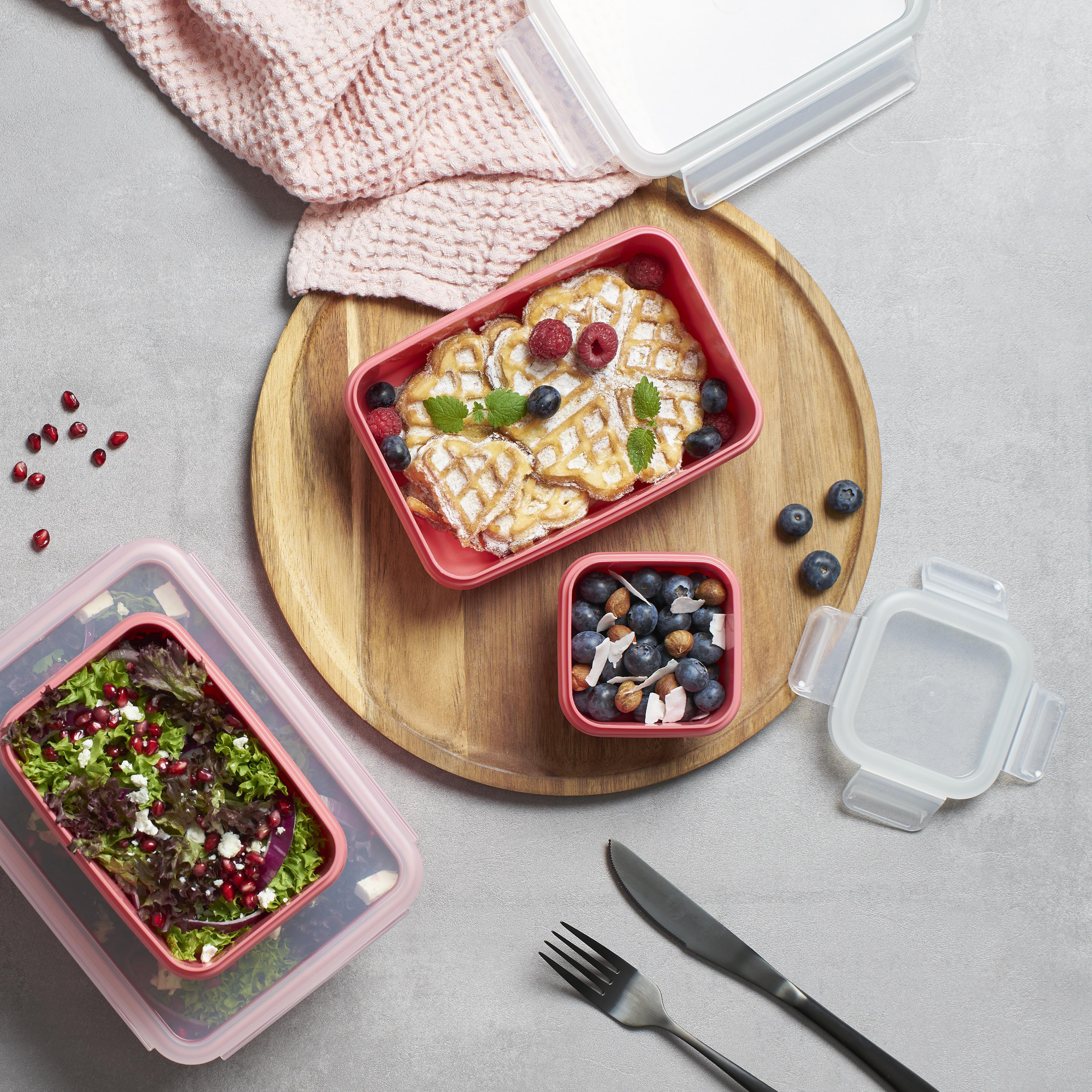 Lebensmittelbehälter mit Waffeln, Salat und Blaubeeren auf einem Holzbrett, mit Utensilien.