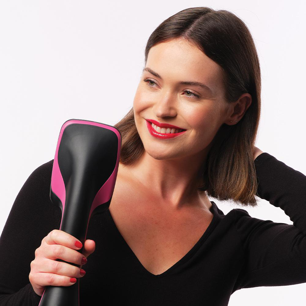 Eine Frau mit rotem Lippenstift hält ein Haarstyling-Werkzeug und lächelt nach rechts.