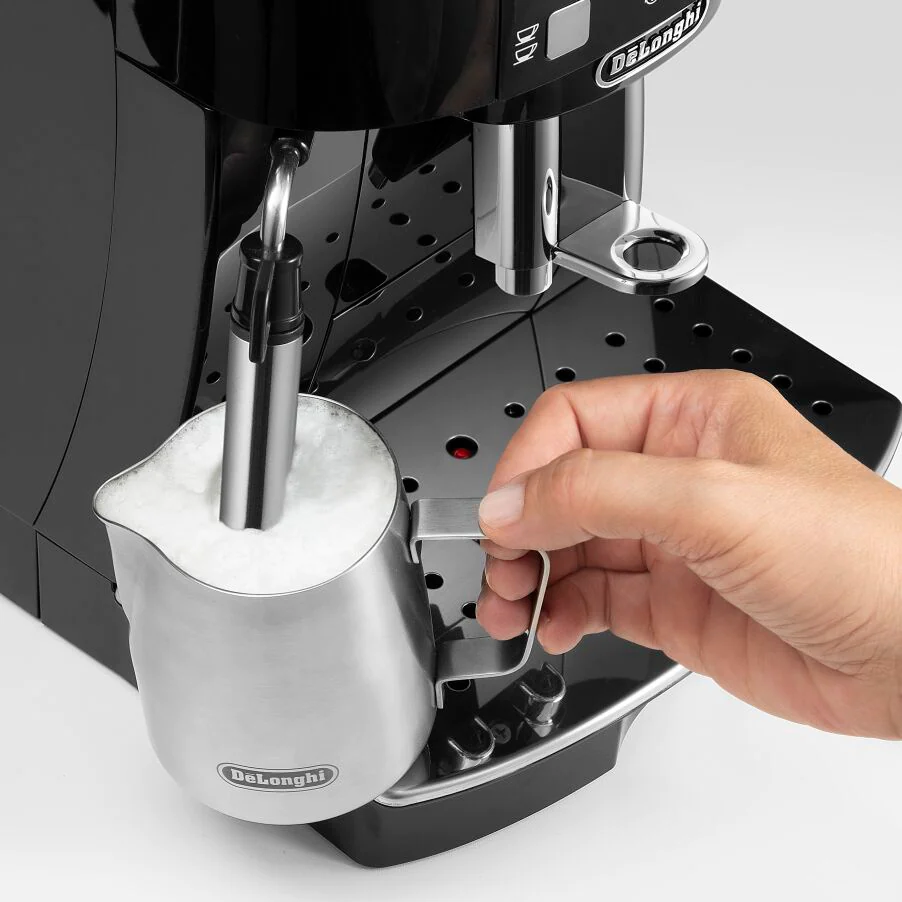 Une main verse du lait dans une pichet à mousse de lait en acier inoxydable.