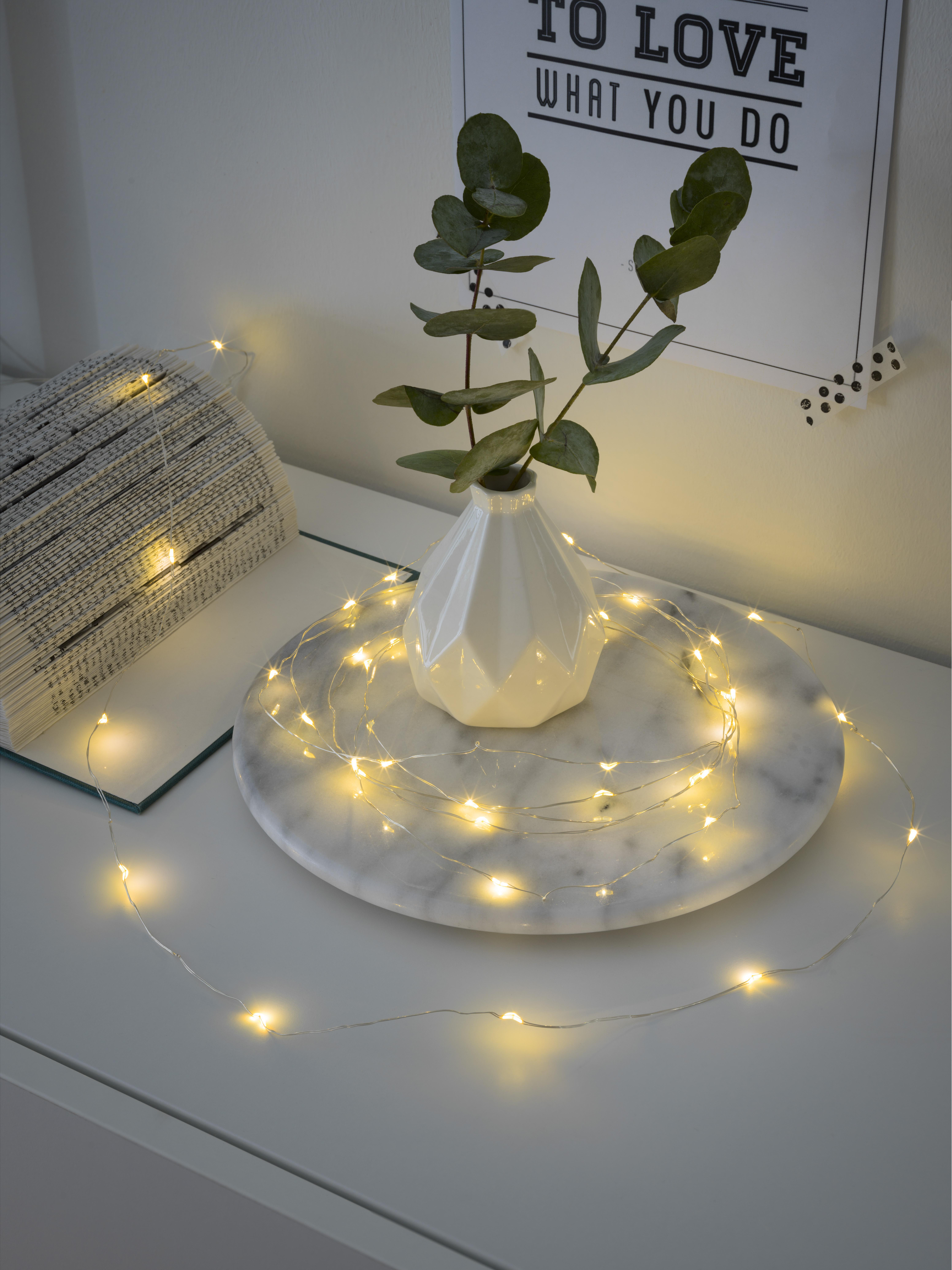 Weiße Vase mit Eukalyptus, Lichterkette auf Marmortablett mit Buch.