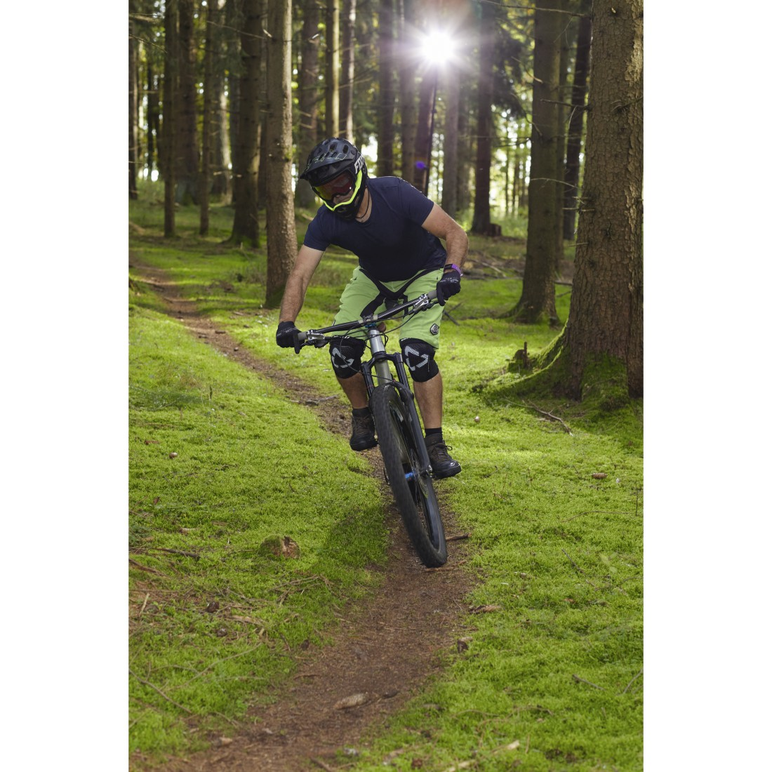 Mann fährt Mountainbike auf einem Waldweg. Grünes Gras und Bäume herum.