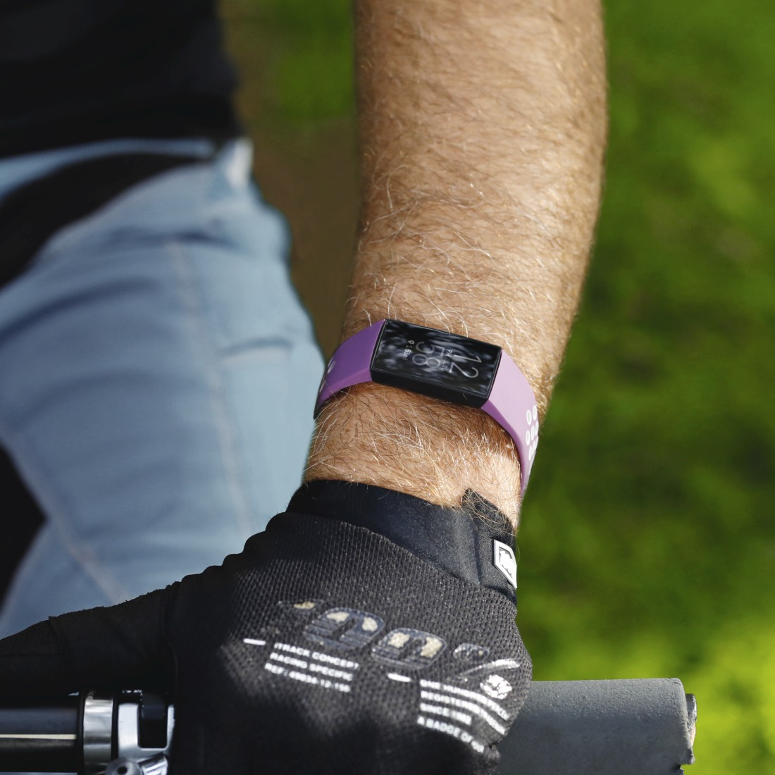 Das Handgelenk einer Person mit einem lila Fitnesstracker und einem schwarzen Handschuh.