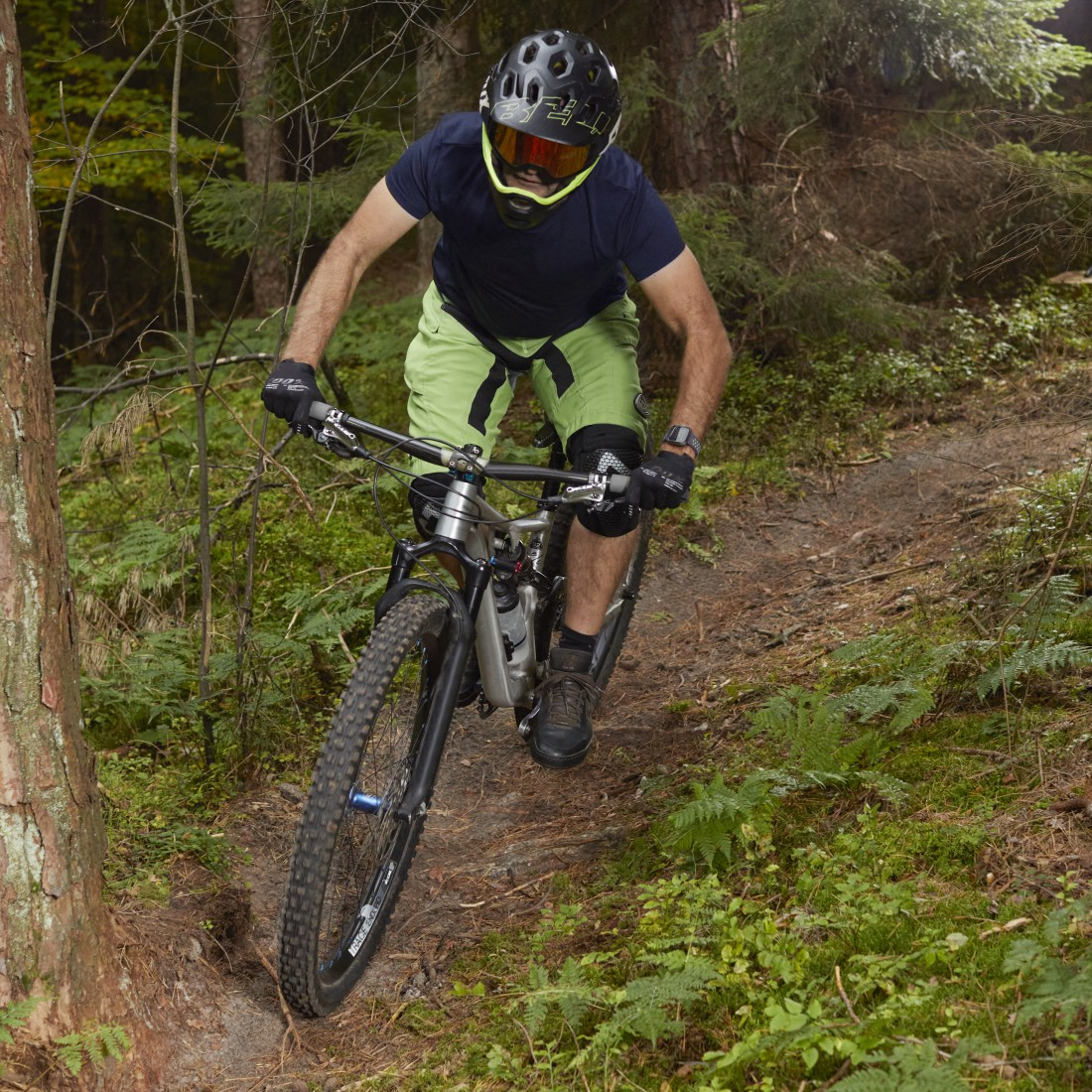 Mann fährt Mountainbike auf einem Waldweg. Helm und Schutzkleidung. Grünes Laub.