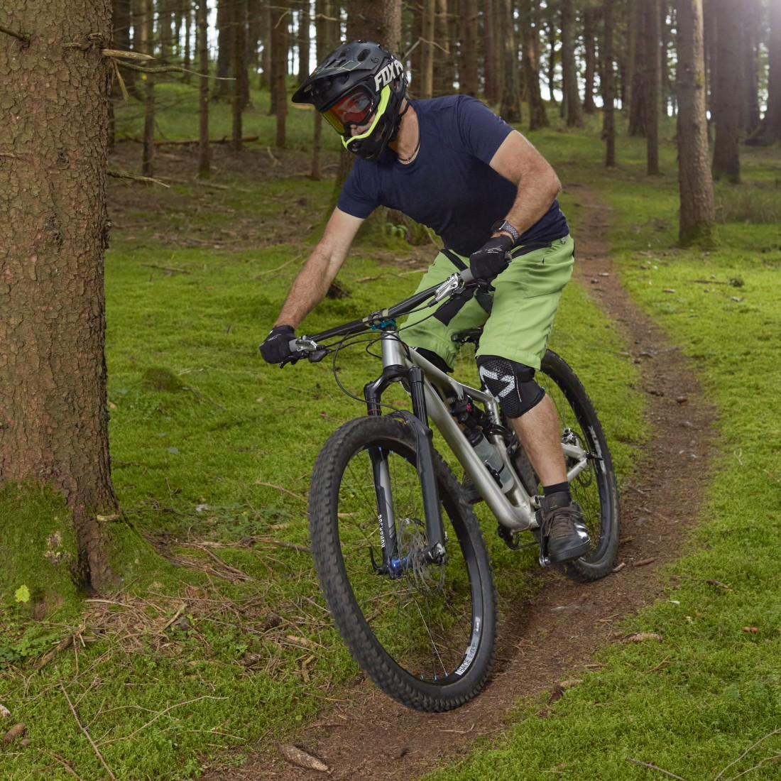 Eine Person fährt mit einem Mountainbike auf einem Waldweg. Sie trägt Helm und Schutzkleidung.
