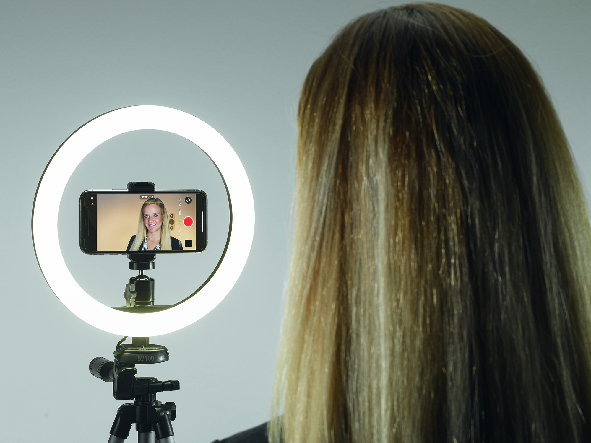 A woman filming herself with a phone in a ring light.