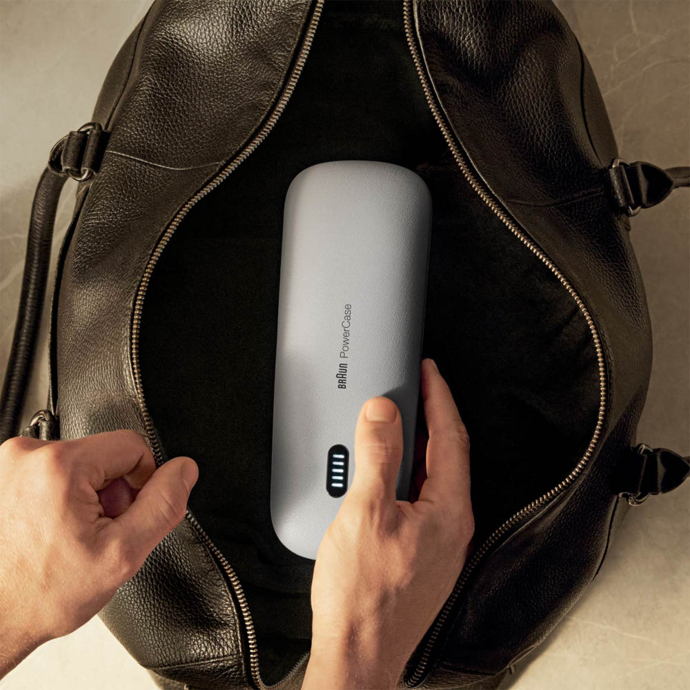 Hands opening a black leather bag to reveal a light gray Braun PowerCase.