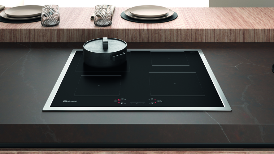 Schwarzes Kochfeld mit einem Topf darauf. Edelstahlverkleidung um das Kochfeld.