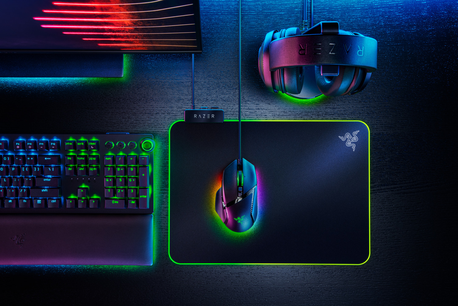 Gaming-Setup mit Razer-Tastatur, Maus, Mauspad und Headset. Schwarzer Schreibtisch mit bunten Lichtern.