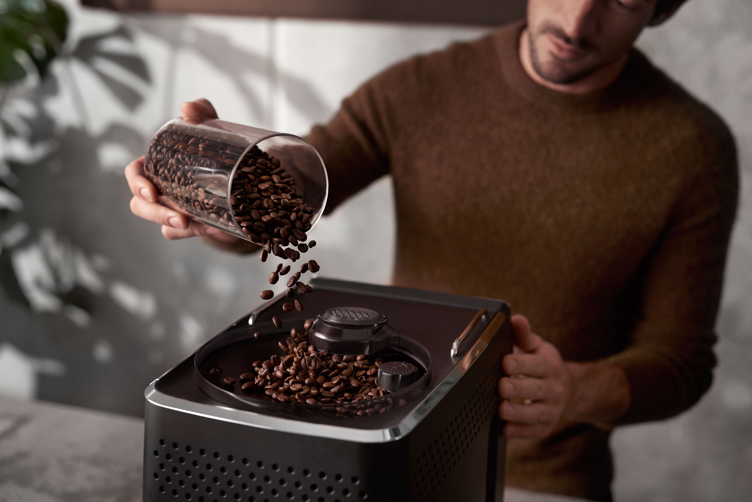 Un uomo versa chicchi di caffè in una macchina da caffè da un barattolo.