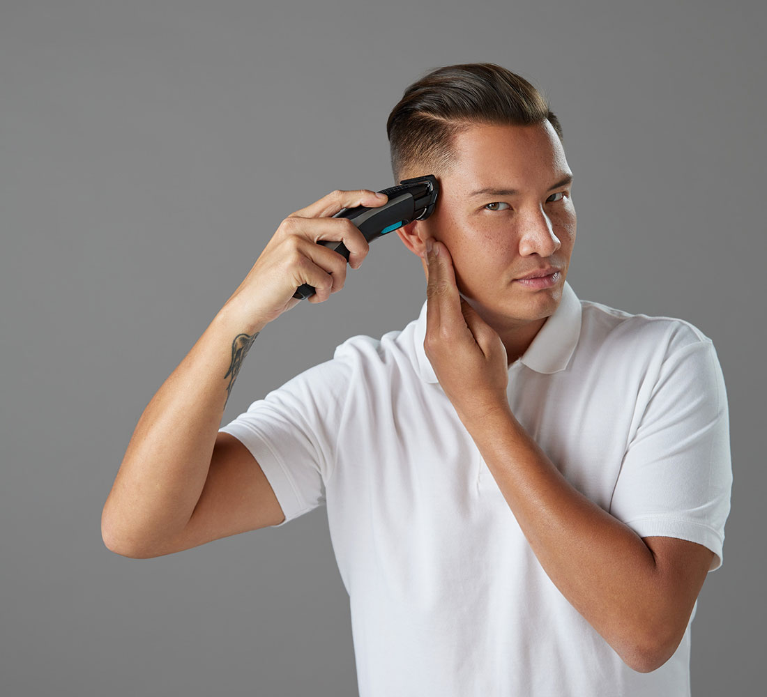 Mann im weißen Hemd benutzt einen Trimmer für sein Haar, grauer Hintergrund.