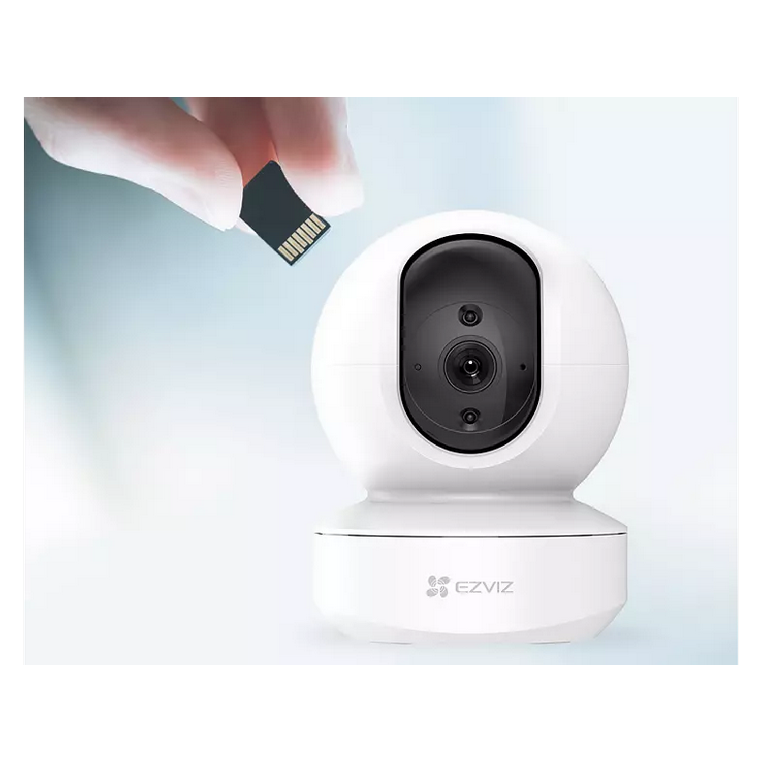 Cámara de seguridad EZVIZ blanca y tarjeta microSD. Mano sosteniendo la tarjeta. Fondo azul claro.