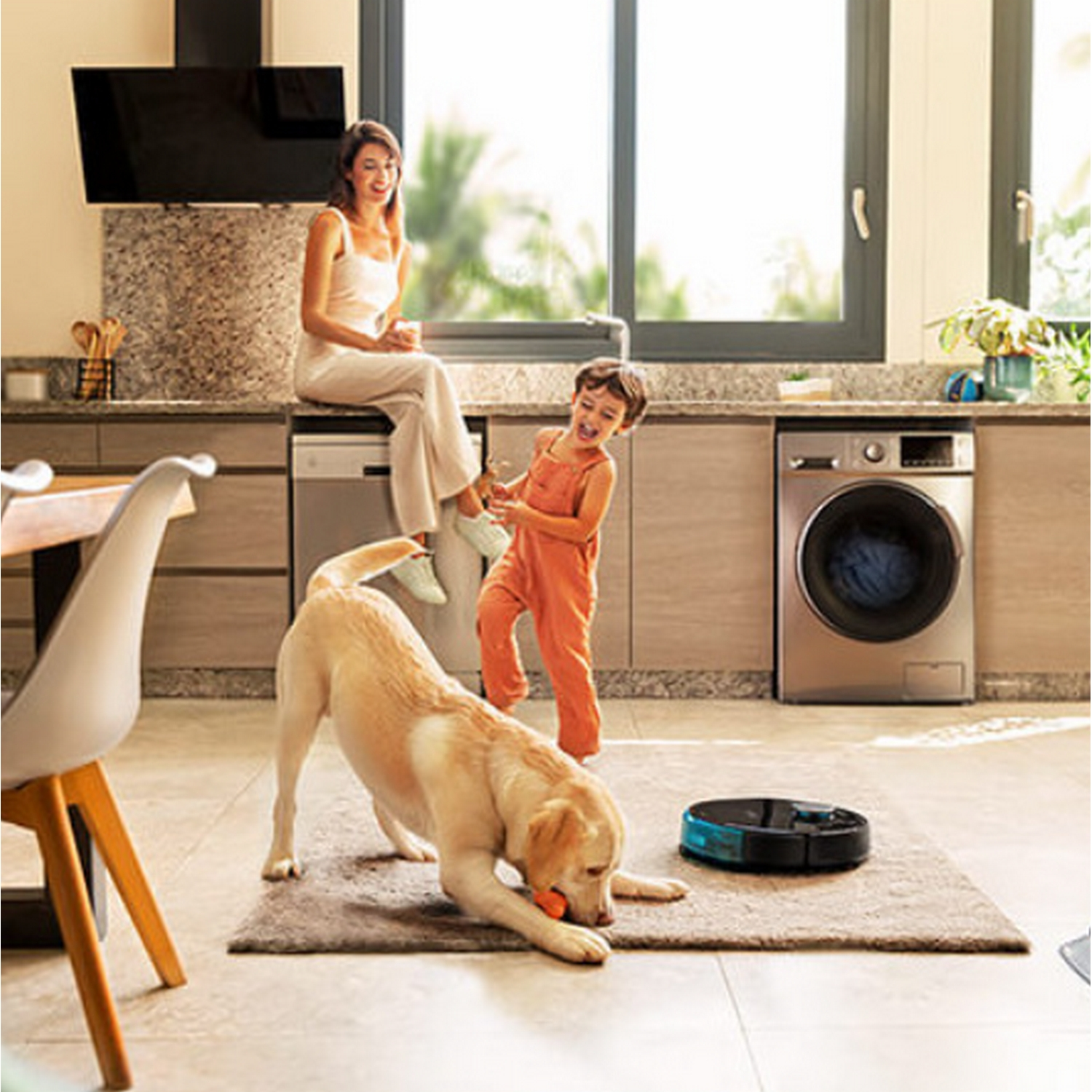 Una familia en una cocina. Un perro juega con un juguete. Hay un robot aspirador.