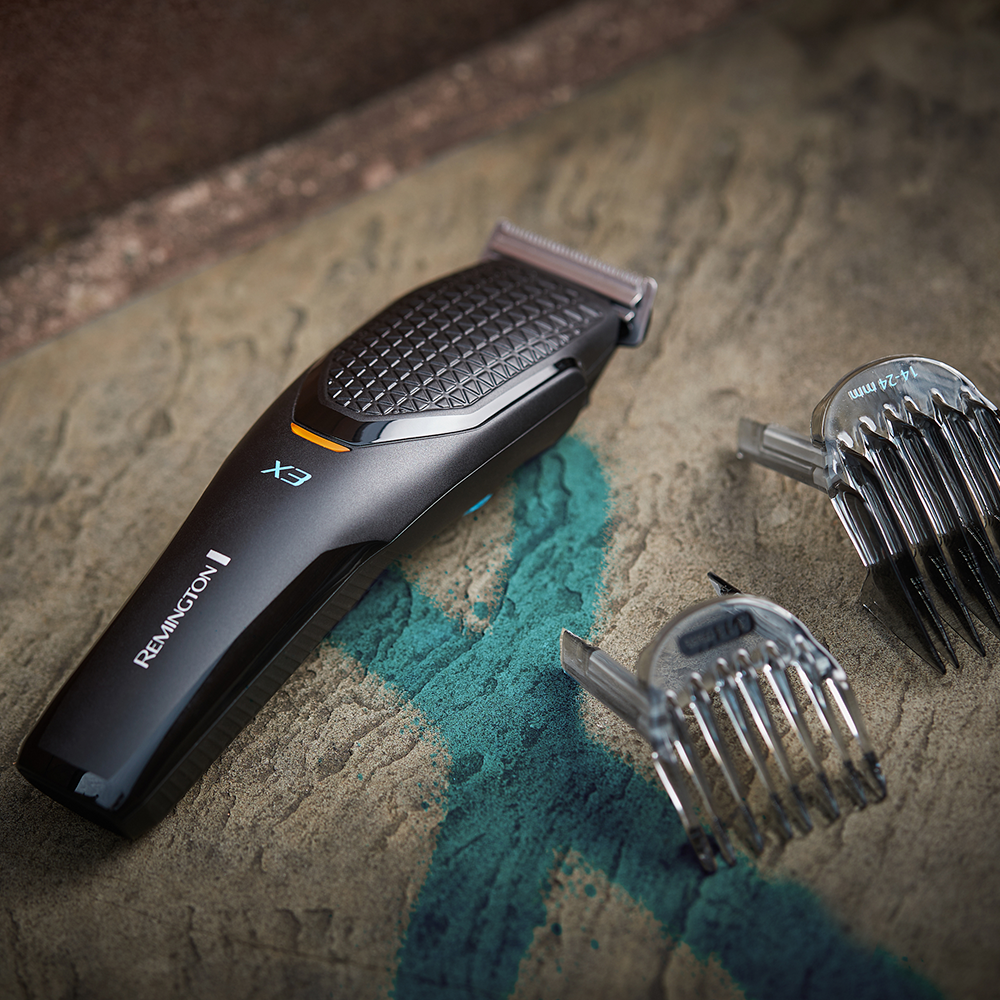Ein schwarzer Remington EX Haarschneider mit drei Kammaufsätzen. Der Trimmer liegt auf einer Steinoberfläche.