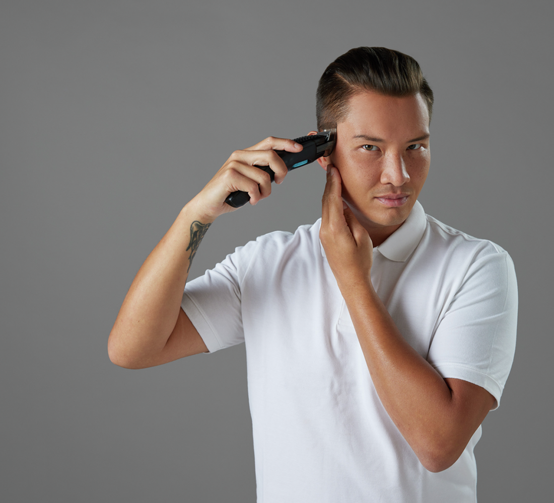 Ein Mann rasiert sich mit einem elektrischen Rasierer die Haare. Er schaut in die Kamera.