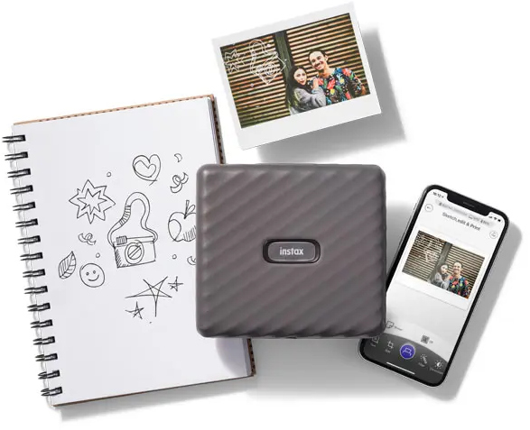 Instax printer with a notebook, photos, and a smartphone displaying an image.