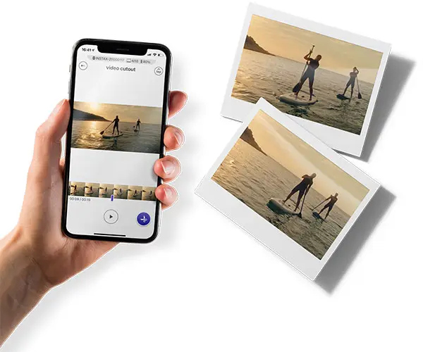 Hand holding phone showing video of people on paddleboards, polaroid photos next to it.