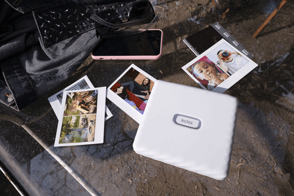 Photos, smartphone, and a white printer on a textured surface. Clothing in the background.