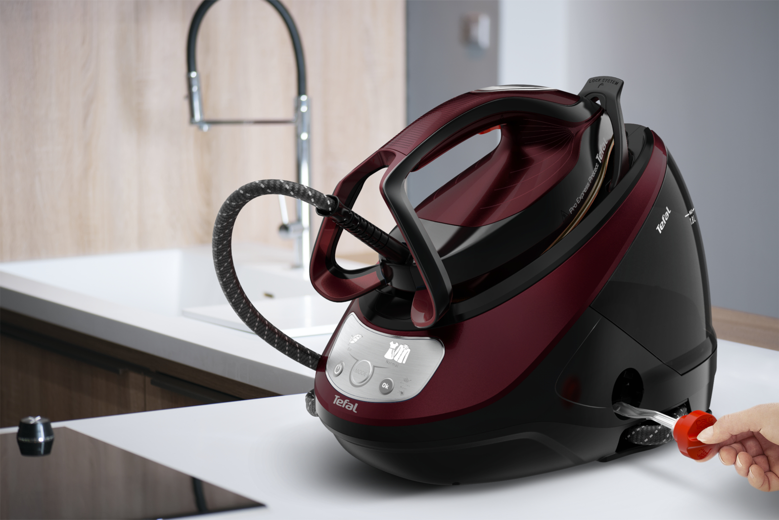 Kırmızı ve siyah bir Tefal buharlı ütüsü, bir el kablo tutuyor ve bir mutfak arka planı.