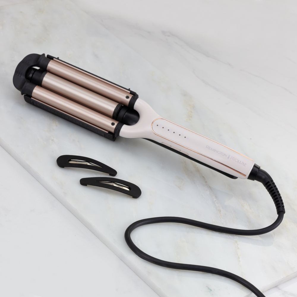 Un fer à onduler Remington Proluxe et deux pinces à cheveux sur une surface en marbre.