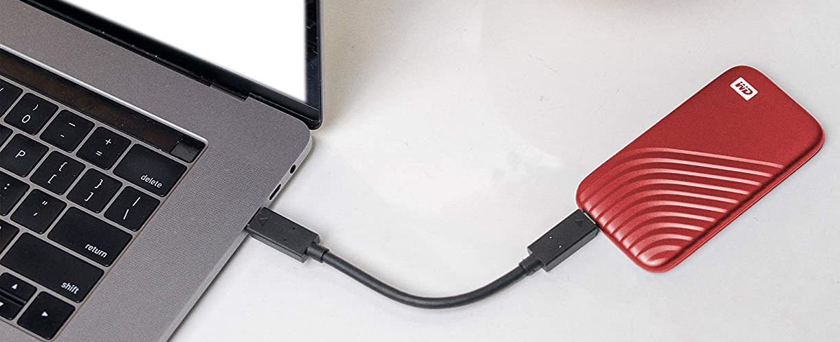 Egy laptop egy piros WD külső merevlemezhez csatlakoztatva, fehér felületen.