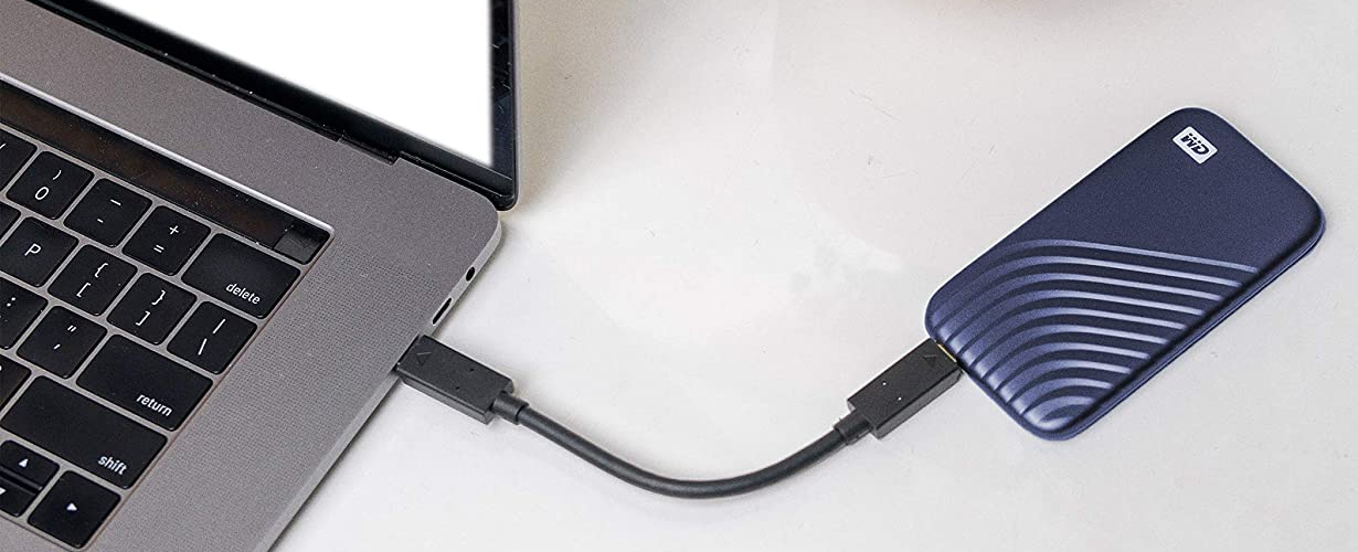Laptop egy hordozható merevlemezhez csatlakoztatva USB-kábellel. A beállítás egy fehér asztalon van.