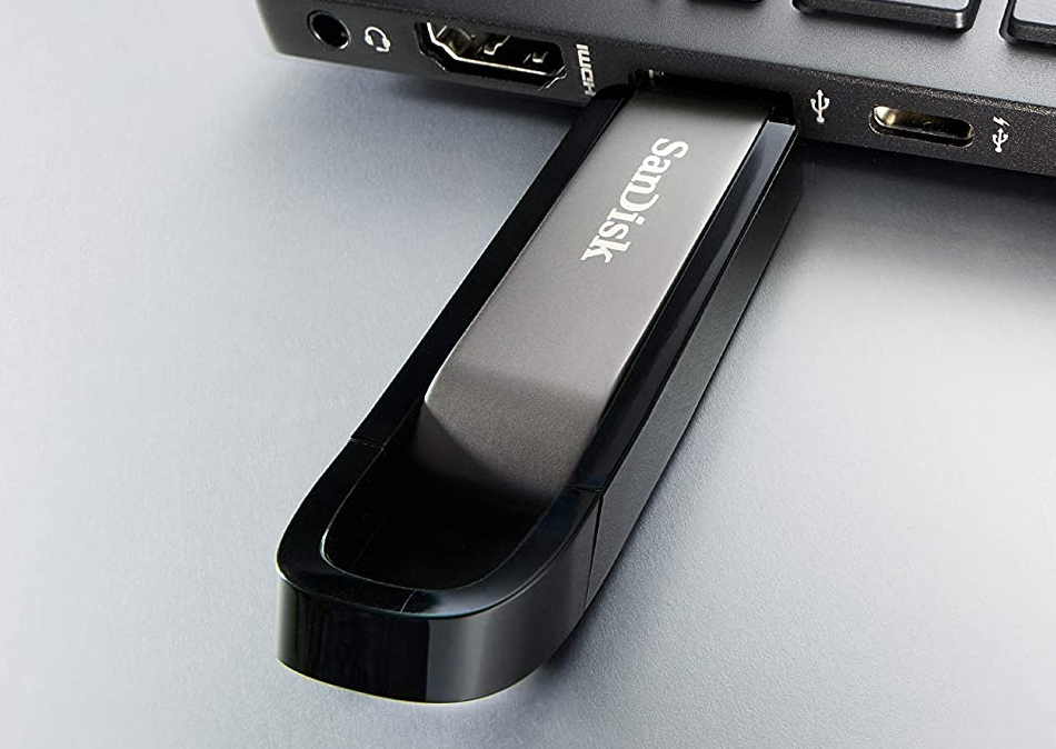 USB-meghajtó egy laptopba helyezve. A meghajtó szürke és fekete, a márka a SanDisk.