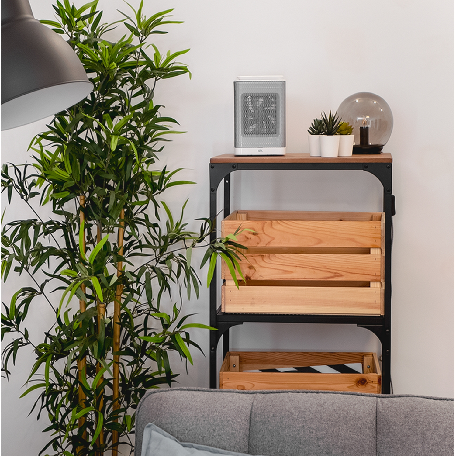 Un estante de madera con una planta, una lámpara y cajas de madera. Un sofá gris en primer plano.