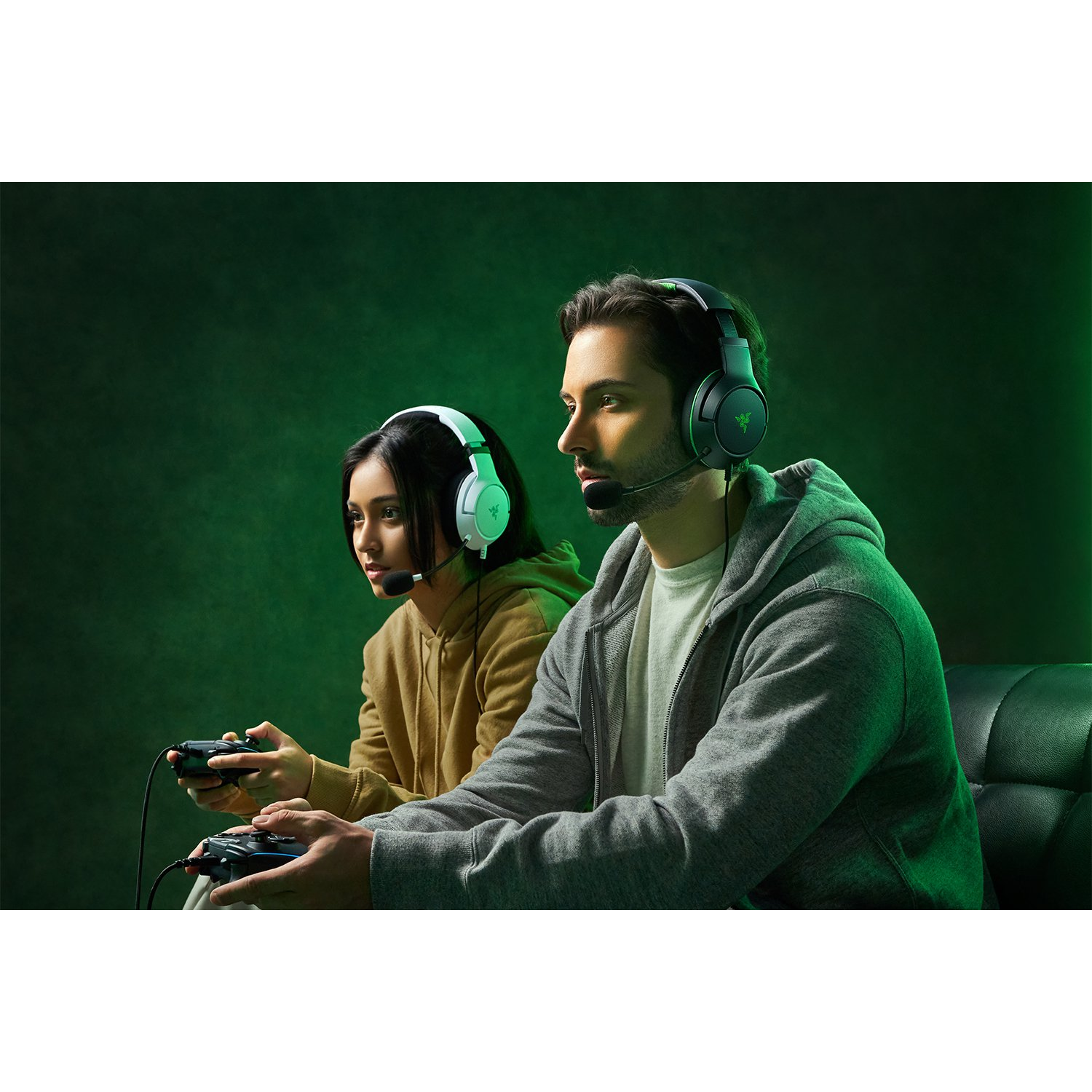 Dos personas con auriculares jugando videojuegos. Fondo verde. Los controladores son visibles.