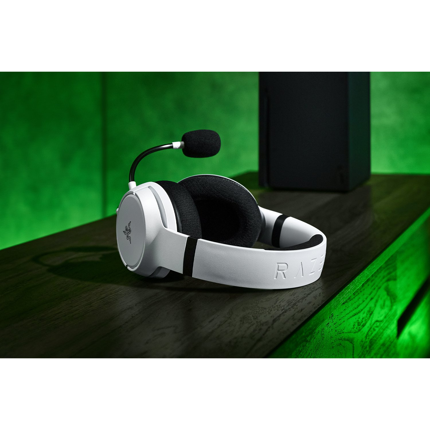 Auriculares gaming blancos con micrófono, sobre mesa de madera oscura, fondo verde.