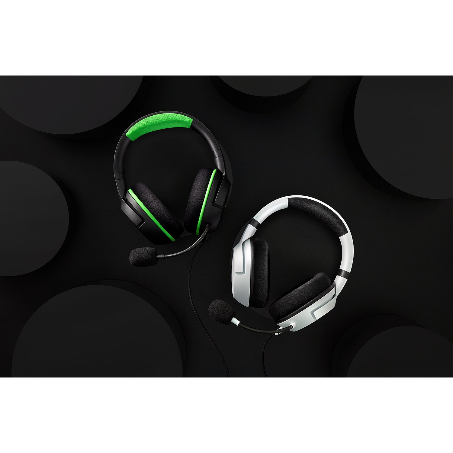 Dos auriculares gaming negros con micrófonos sobre una superficie negra con círculos negros.