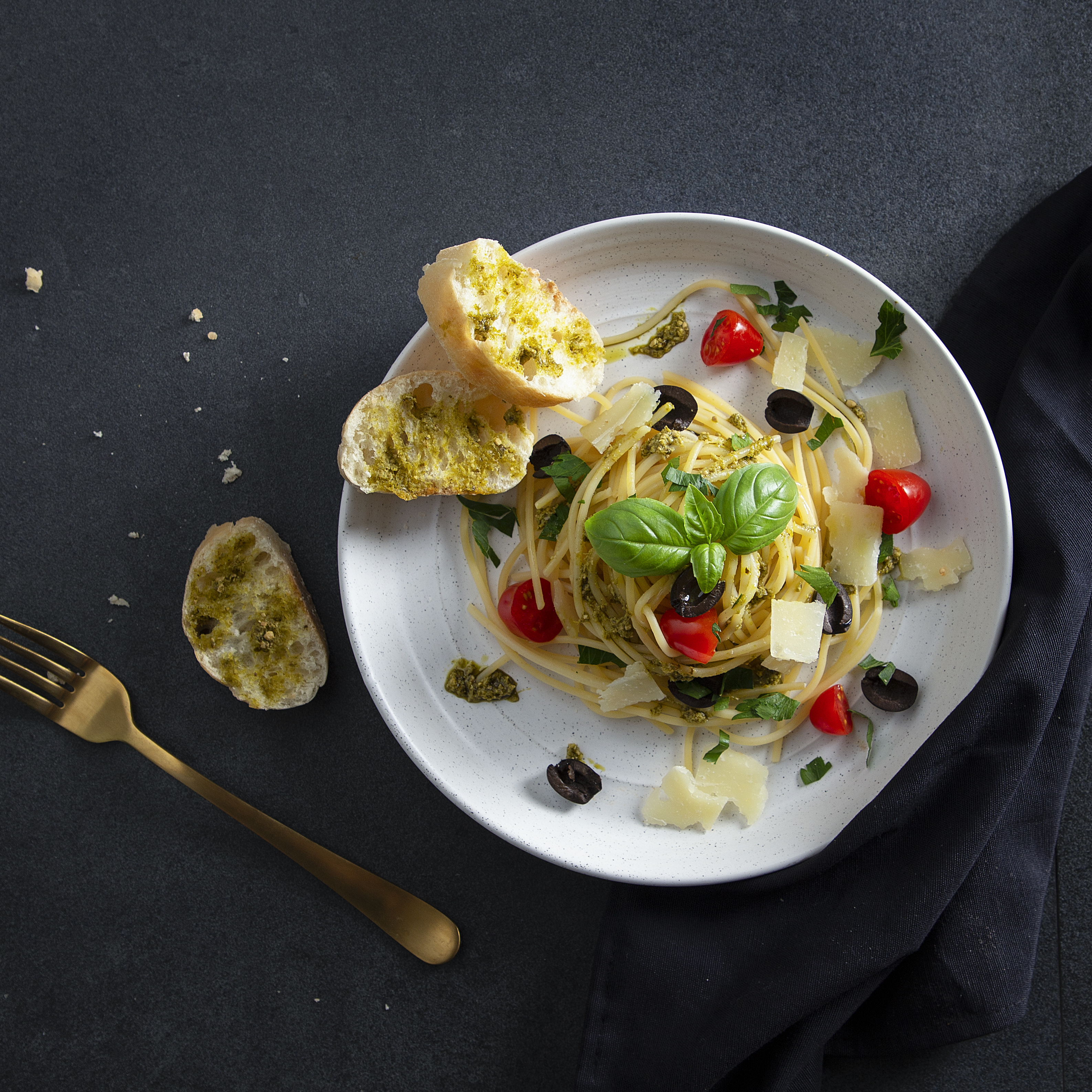 Spaghetti met pesto, tomaten, olijven en kaas op een bord.