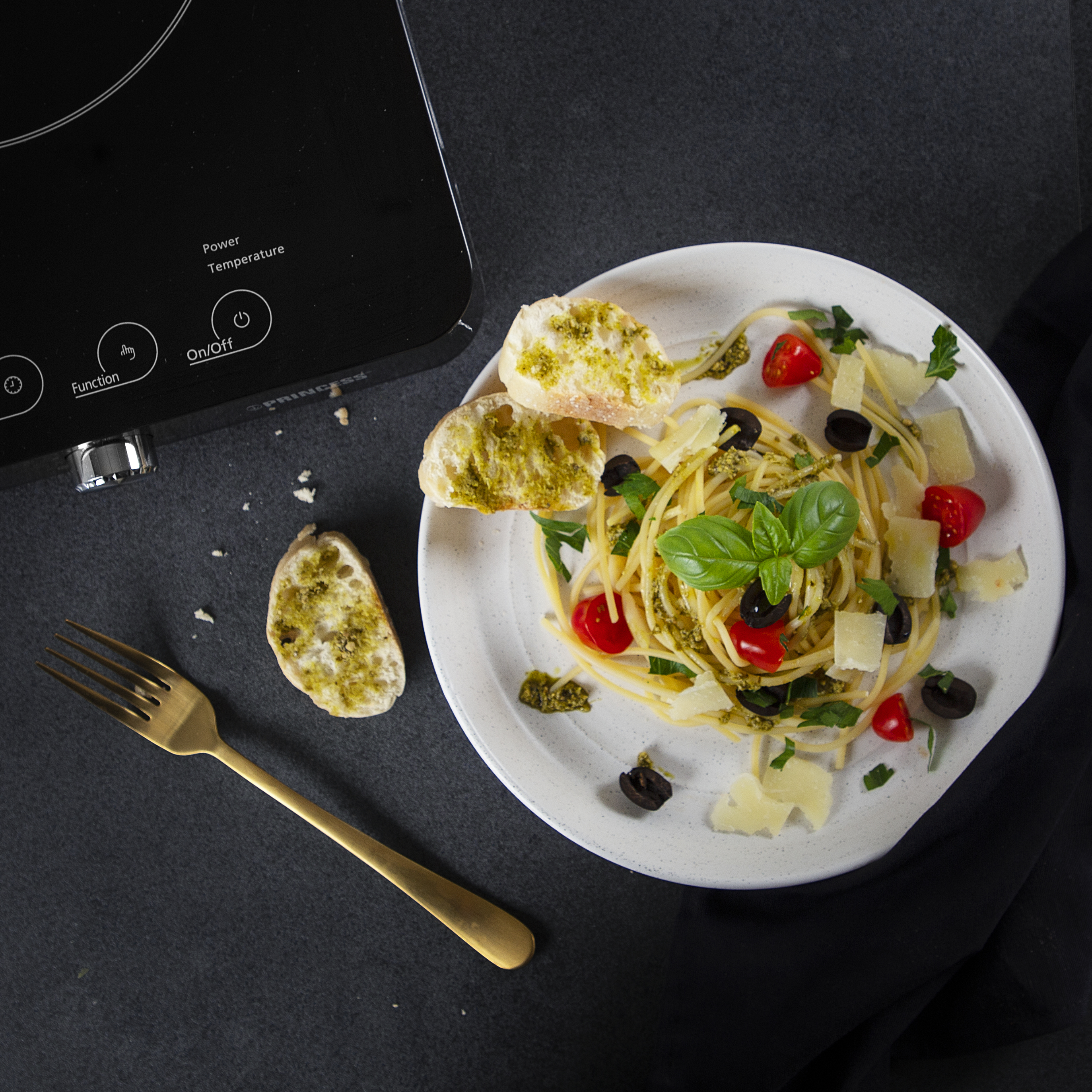 Pastagerecht met pesto, tomaten, olijven, basilicum en Parmezaanse kaas. Gouden vork en zwart oppervlak.