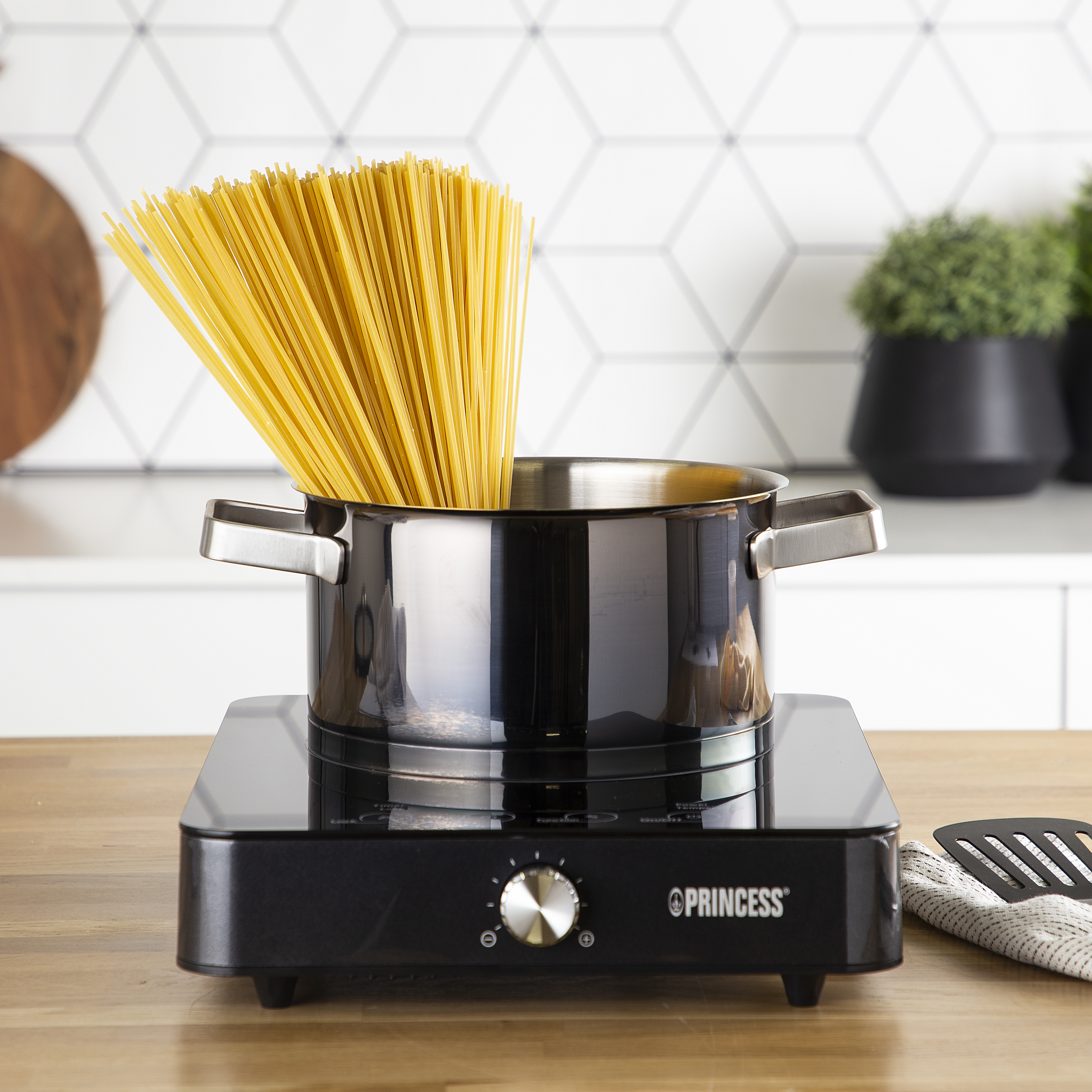 Een pot op een inductiekookplaat met spaghetti die uit de pot komt.
