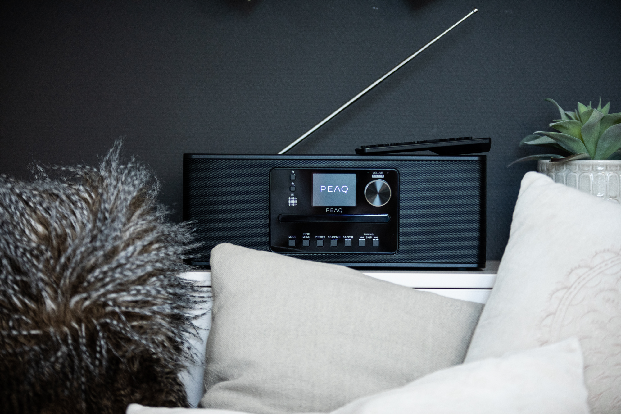 Une radio PEAQ noire avec antenne et télécommande est sur une étagère.