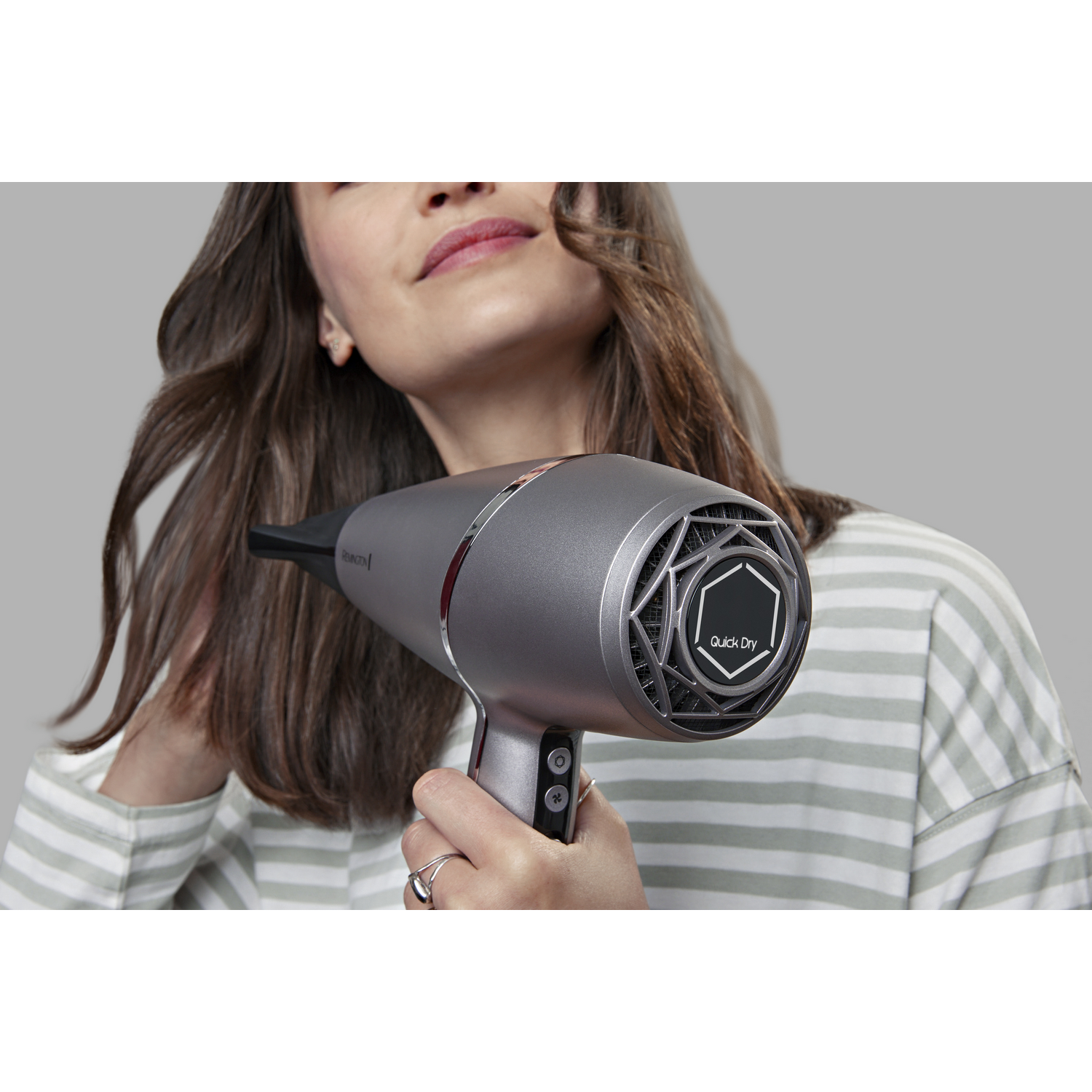 Mujer secando su cabello con un secador de pelo gris Remington Quick Dry sobre un fondo gris.